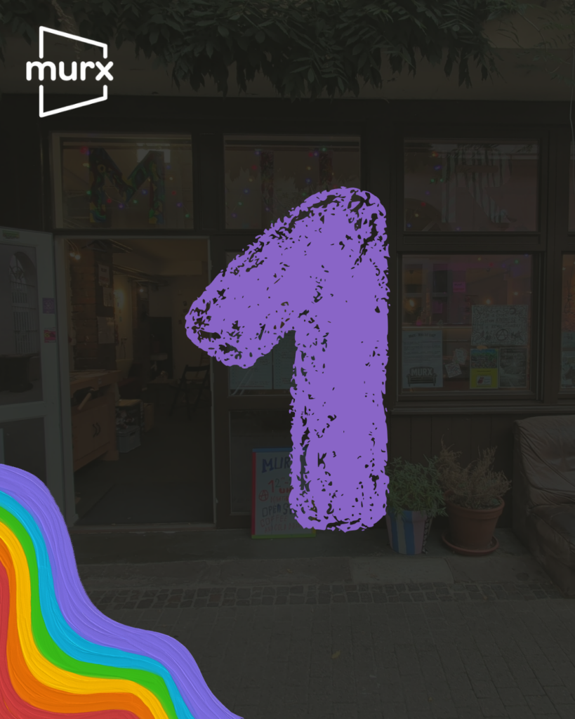 Bild in dessen Hintergrund ein etwas abgeblendetes Bild des Murx von Außen ist. | Links oben das Murx-Logo, Links unten ein Regenbogen in Pastellfarben, in der Mitte eine große 1 die wie mit Kreide geschrieben aussieht.
